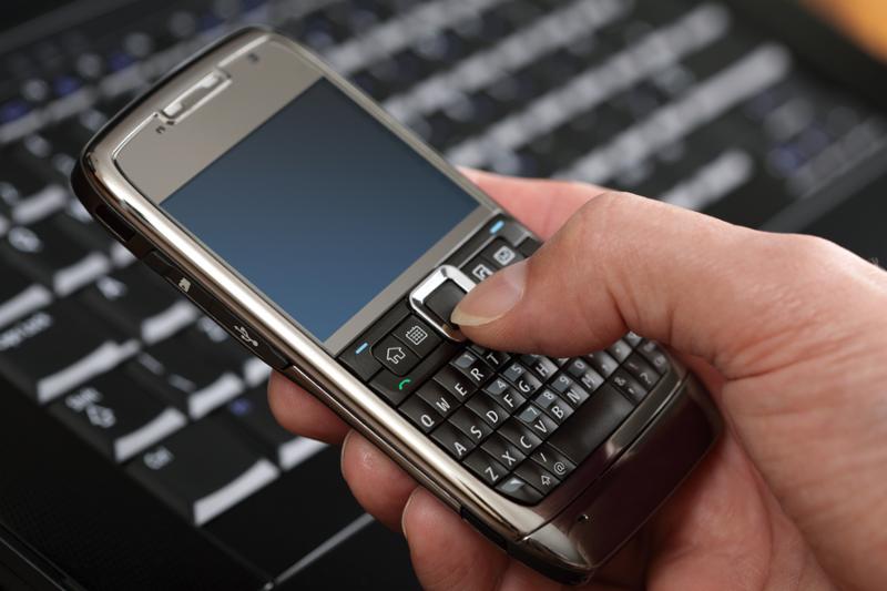 Using a PDA mobile phone with laptop keyboard background, blank screen for copy